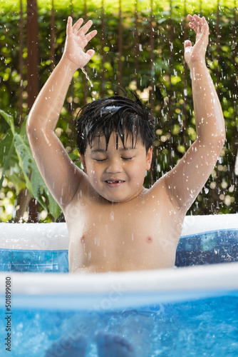 Portrait of a boy playing in the inflatable pool at his home. Cool summer activities. © wacharaphong