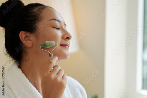 Fotografía Young Asian woman enjoying massage with jade face roller in the morning