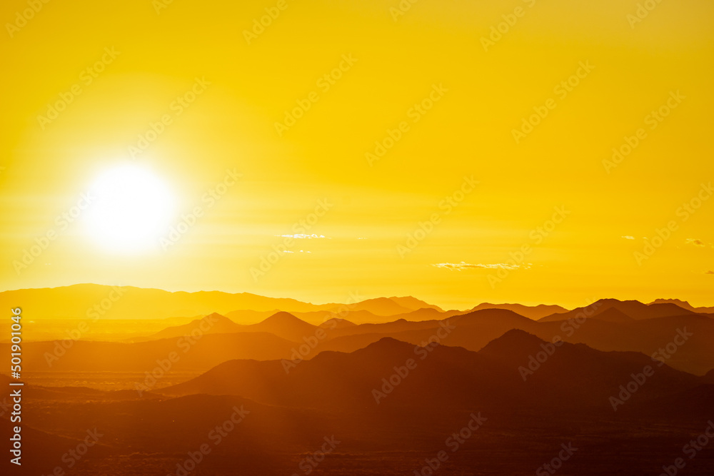 The sun setting behind the mountains of the Sonoran Desert in Arizona with the air lit up in golden light with mountains in silhouette.