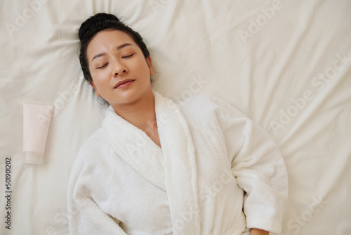 Young woman fell asleep on bed after taking relxing hot bath and applying lotio photo