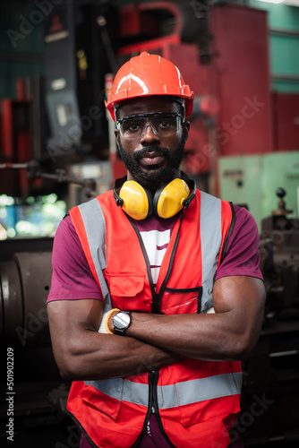 portrait of sober and determined eyes african-american man worker have unkempt beard in safety uniform wearing helmet,glasses, vest and glove in industrial manufacturer factory.
