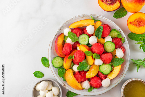 Fruit summer salad made of fresh fruits  mozzarella cheese  cucumbers and mint on white table. top view