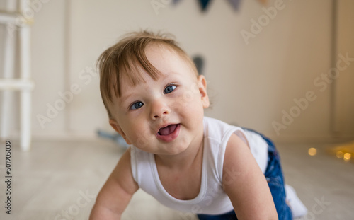 portrait of a baby boy with a squint crawling on the floor in the nursery