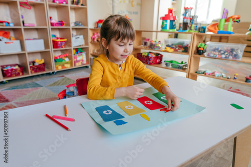 Obraz na plátně Little girl playing with poster of garbage containers for sorting at kindergarte