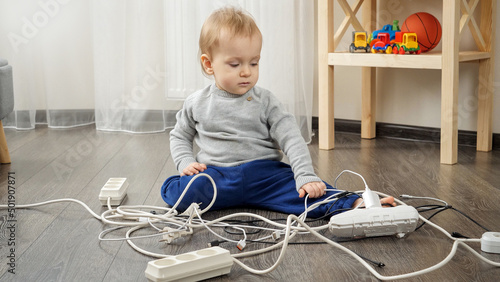 Little baby boy left alone playing with electric cables and wires. Child in danger photo