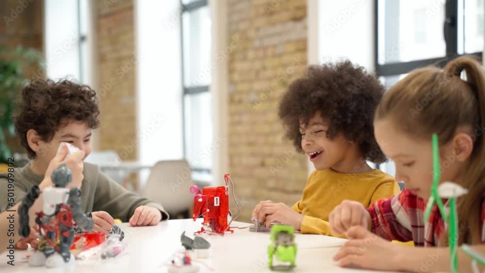 Concentrated kids learning how to build robotic toys and programming them using computer during STEM class with young female teacher