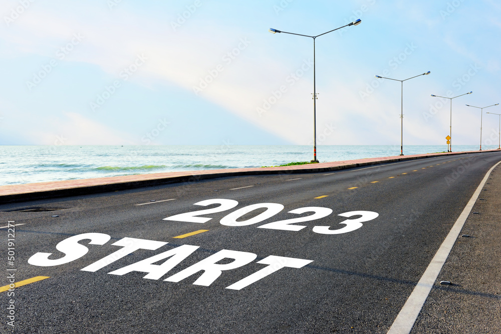 Fototapeta premium Start new year 2023 on asphalt road with marking line for given direction and sea landscape. Road to recovery concept and business success idea
