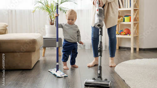 Little baby boy helping his mother doing cleanup at home and vacuming carpet.