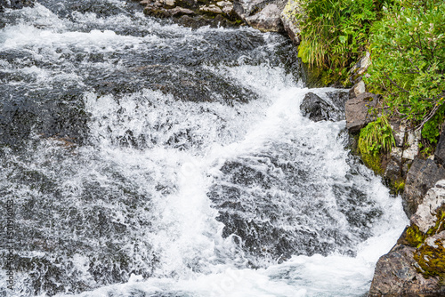 Turbulent spring stream of mountain river. Water foams  breaks into splashes on stones. Power of nature  continuous movement and energy.