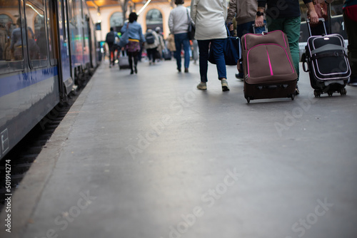 Foule de gens qui marchent dans le même sens sur le quai d'une gare à côté d'un train pour un départ en vacances ou bien pour aller au travail