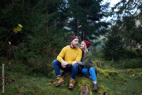 Young couple in love sitting in forest together. Carpathian mountains travel in Ukraine. Two tourists spending relaxing time in the woods. Romantic relationship of young people.