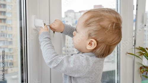 Little baby boy opens window safety lock with key. Baby in danger. Child safety and protection