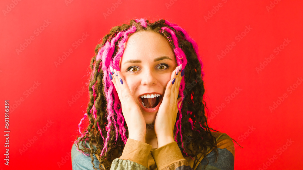 Young surprised woman leaning hands against cheeks and opening mouth on red background. Emotional female looking at camera with pleasant amazement and shocking on face. Young surprised woman leaning hands against cheeks and opening mouth on red background. Emotional female looking at camera with pleasant amazement and shocking on face.