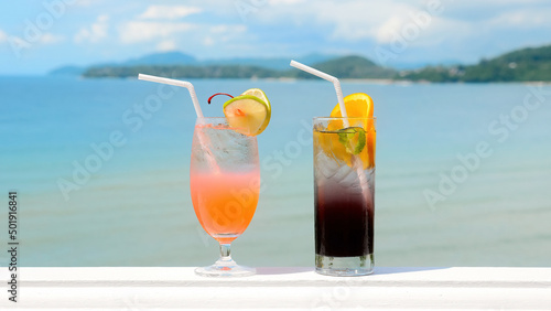 Two glasses of chilled non-alcoholic tasty tropical cocktails with slices of orange and lime in hot summer sunny day with ocean on background. Close-up of refreshment mocktails. Travel concept