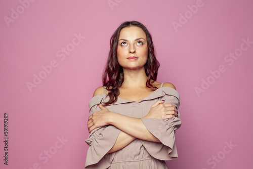 Nice woman looking up and standing with crossed arms on pink background