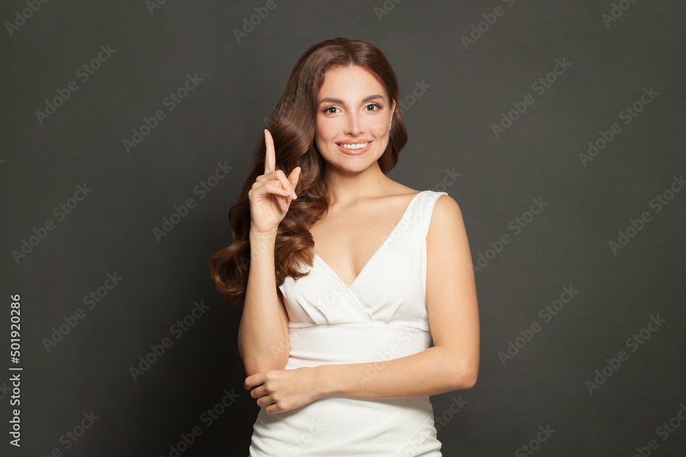 Young beautiful woman with curly hair and clean skin pointing up and smiling on gray studio wall background