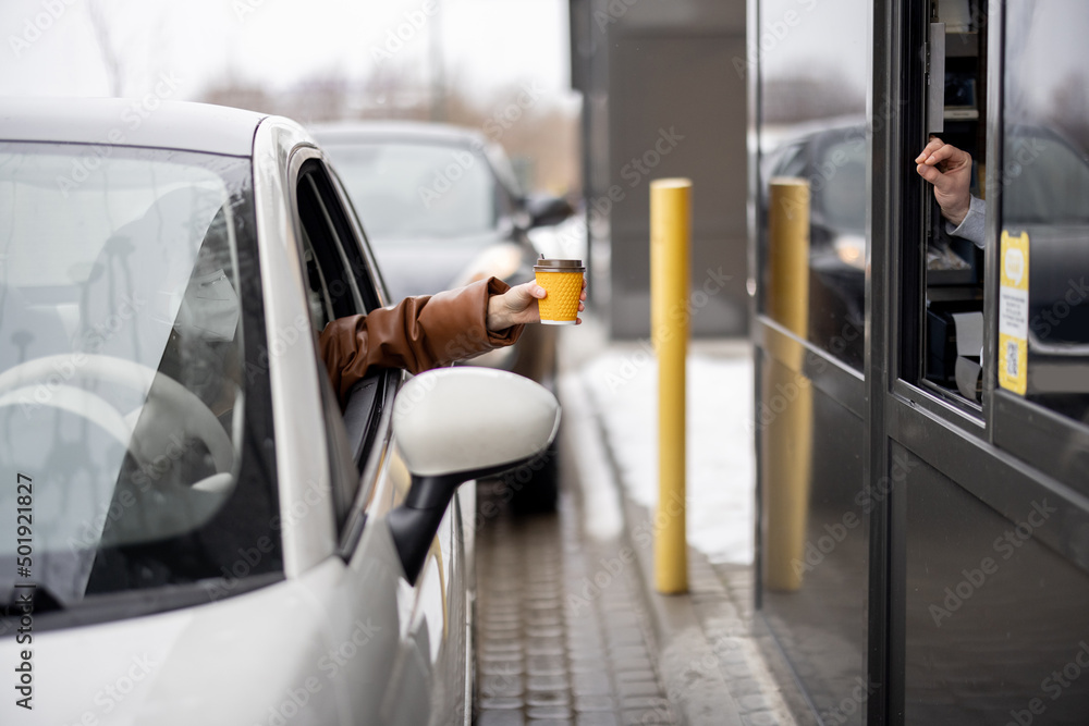 Fototapeta premium Driver takes coffee to go at the point of issuing orders on the go. Fast food and ordering during pandemic concept