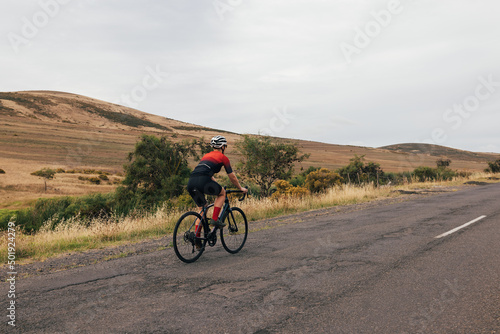 Back view of sportswoman cycling road bike on empty countryside road