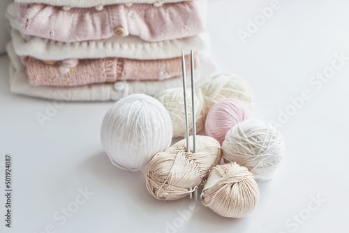 Stack of knitted clothes and balls of yarn, knitting needles, accessories for knitting. Baby clothes. Needlework, hobby, knitting, handwork.