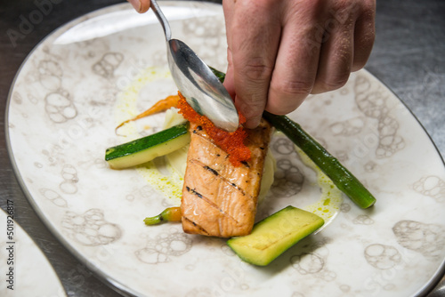 Manos de cocinero realizando un emplatado con salmón y verduras photo