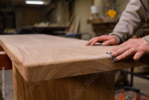 Closeup of person sanding wooden table using sandpaper in workshop