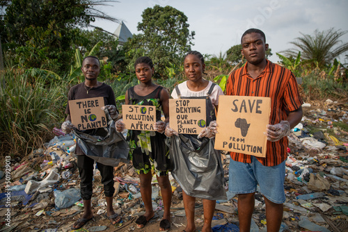 A group of young African activists protest with signs against pollution, they are in front of an illegal landfill and they are about to remove the waste