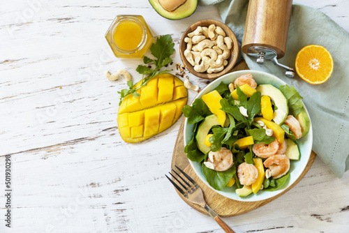 Vegetarian vegan healthy food. Salad with arugula, mango, avocado, shrimp, pecans and dressing of olive oil, honey and wine vinegar on a rustic kitchen table. Top view, flat lay. Copy space.