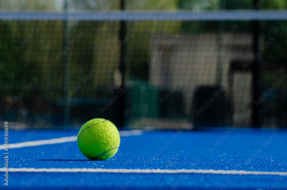 Padel tennis ball on a blue court with the net out of focus in the background. Racket sports concept.