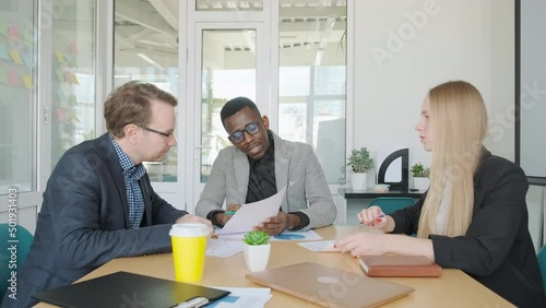 Meeting of creative multiracial business team in office. International multi-ethnic teamwork, working with papers, discussing and analyzing data with graphs and diagrams. Ethnic and gender diversity