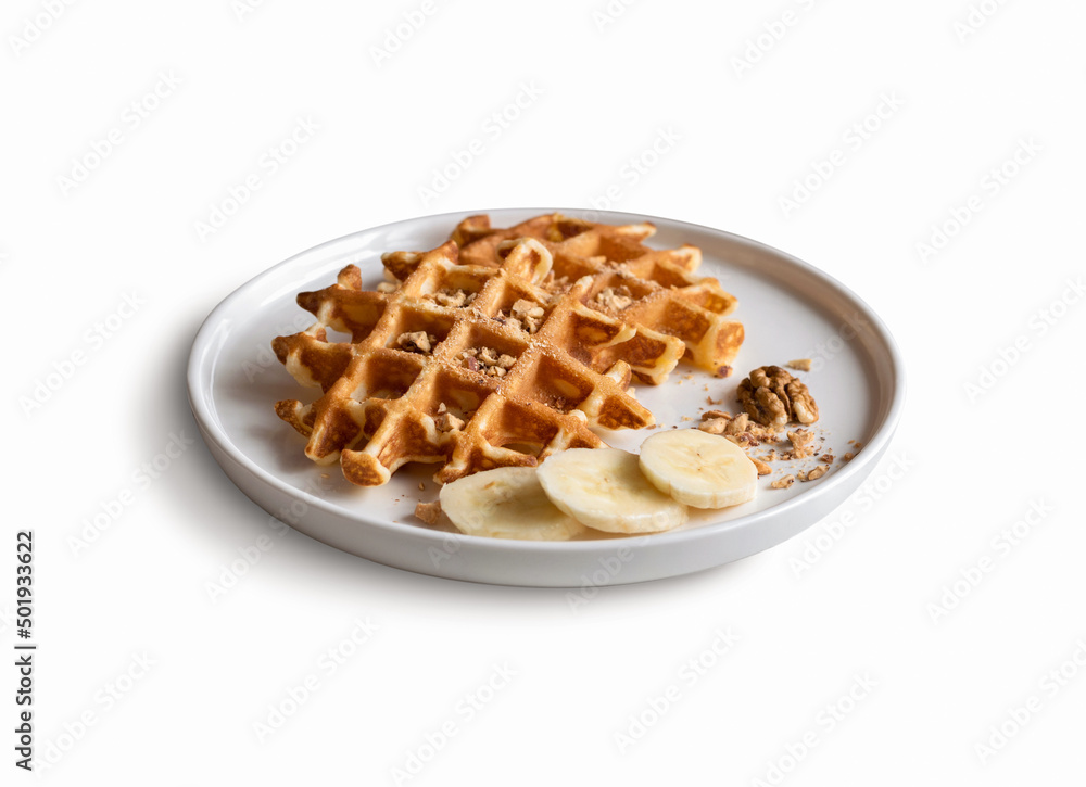 Belgian waffles with chopped nuts and pieces of banana on a plate, isolated on a white background. Close-up. Belgian waffles with chopped nuts and pieces of banana on a plate, isolated on a white background. Close-up.