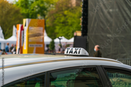 The inscription TAXI on the white roof of the car in front of a blurred background of a man in a medical bandage, a city street and passers-by