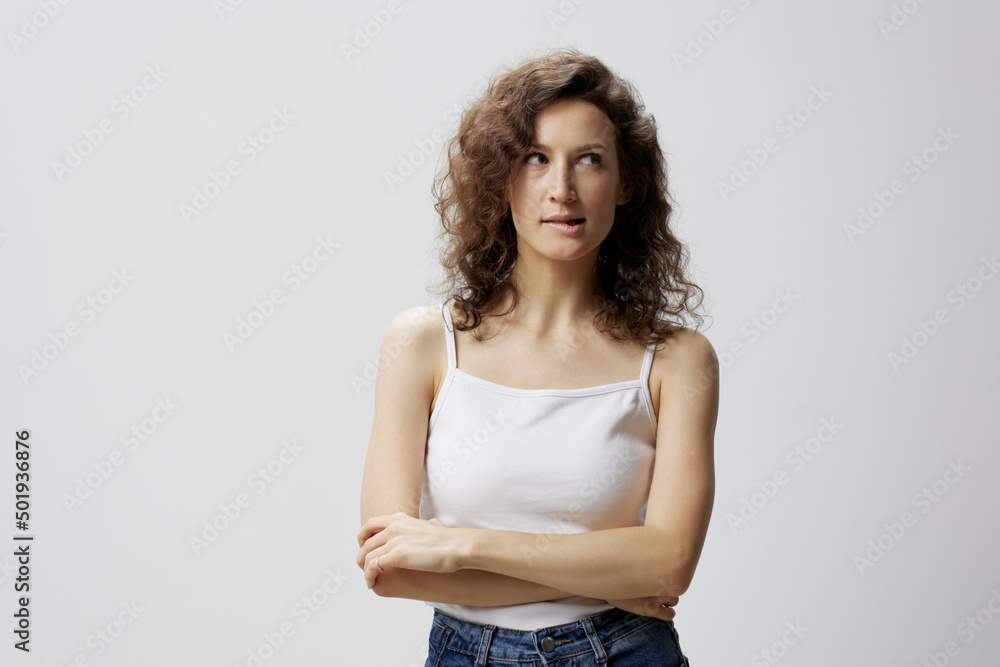Pensive tricky smiling curly beautiful woman in basic white t-shirt looks aside posing isolated on over white background. People Emotions Lifestyle concept. Copy space. Closeup portrait in studio Pensive tricky smiling curly beautiful woman in basic white t-shirt looks aside posing isolated on over white background. People Emotions Lifestyle concept. Copy space. Closeup portrait in studio