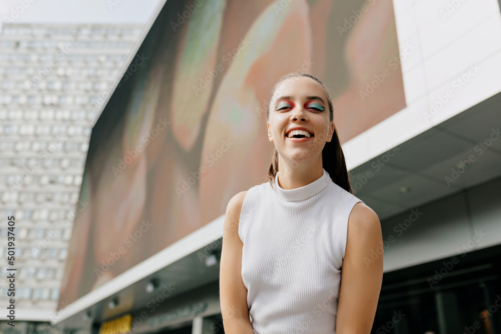 Optimistic cute girl with collected hair in white shirt is smiling sincerely in the city. Cool lady in light blouse with is looking into the camera at street Optimistic cute girl with collected hair in white shirt is smiling sincerely in the city. Cool lady in light blouse with is looking into the camera at street