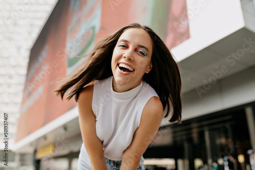 Good humored young woman in stylish summer outfit moves outside and smiles. Happy girl with wonderful smile walks in the city in warm summer day