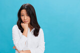 Upset sad cute Asian businesswoman in classic office dress code recline on hand looks at camera posing isolated on over blue studio background. Cool business offer. People Emotions Business concept