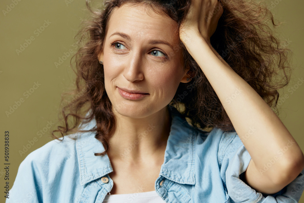 Pensive sad curly beautiful female in jeans casual shirt touch hair looks aside posing isolated on over olive green pastel background. Being Yourself. People Lifestyle emotions concept. Copy space Pensive sad curly beautiful female in jeans casual shirt touch hair looks aside posing isolated on over olive green pastel background. Being Yourself. People Lifestyle emotions concept. Copy space