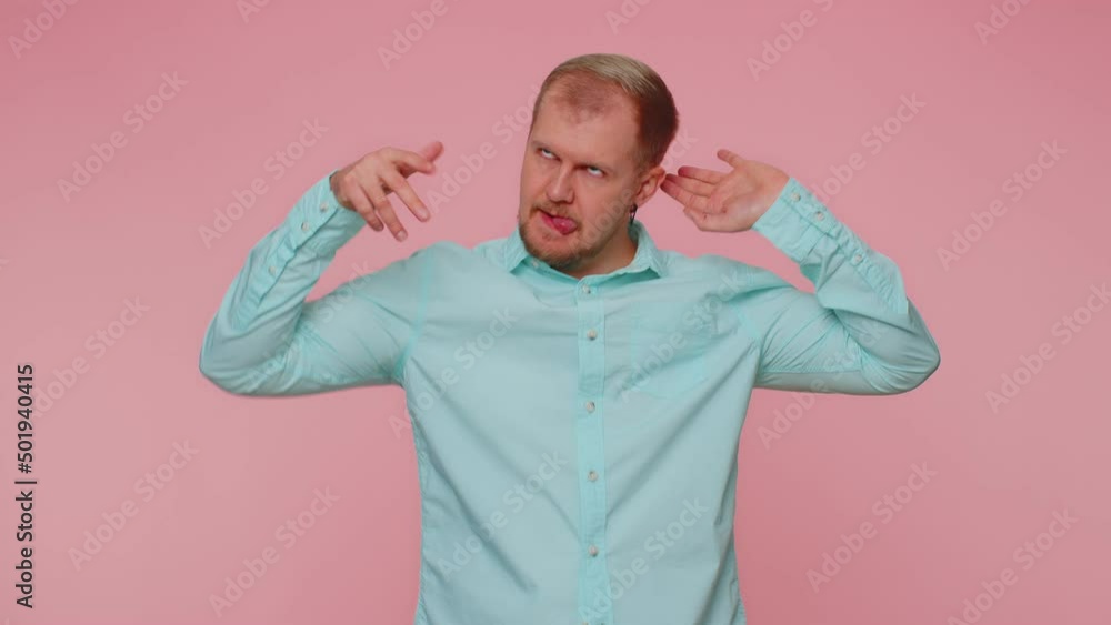 Funny joyful sincere adult man 30 years old in shirt making playful silly facial expressions and grimacing, fooling around showing tongue. Young handsome guy isolated alone on pink wall background Funny joyful sincere adult man 30 years old in shirt making playful silly facial expressions and grimacing, fooling around showing tongue. Young handsome guy isolated alone on pink wall background