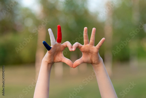 Child hands painted in France flag color forming a heart symbol and love gesture on nature background