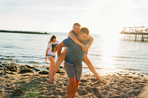 Dad rides his daughter on back on the seashore.  © andrey
