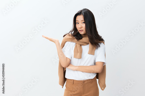 Excited pensive lovely Korean young female in beige warm sweater point hands aside at copy space posing isolated on white studio background. The best offer for ad. Autumn style concept. Seasonal Sale
