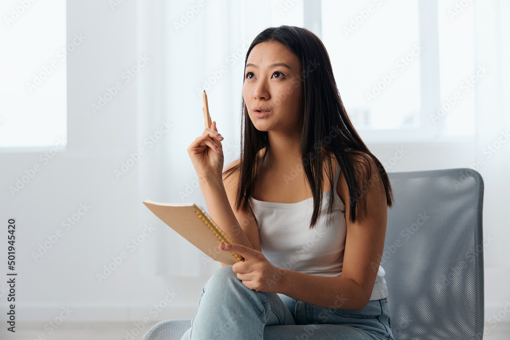 Dreaming excited happy young brunette have cool idea insight holds pen up and notebook in hand looks up at home interior. Writer concept. Copy space Offer Banner. Closeup shot Dreaming excited happy young brunette have cool idea insight holds pen up and notebook in hand looks up at home interior. Writer concept. Copy space Offer Banner. Closeup shot