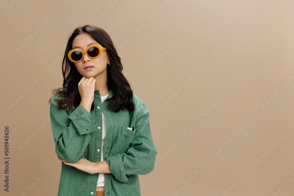 Upset unhappy cute Korean young woman in khaki green shirt stylish eyewear recline on fist posing isolated on over beige pastel studio background. Cool fashion offer. Sunglasses ad concept Upset unhappy cute Korean young woman in khaki green shirt stylish eyewear recline on fist posing isolated on over beige pastel studio background. Cool fashion offer. Sunglasses ad concept