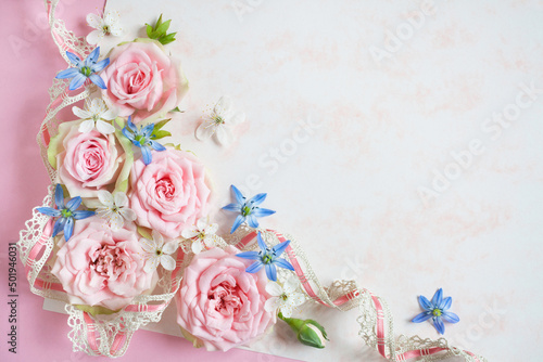 White-pink paper background, pink roses, cherry plum flowers, scilla and lace ribbon, space for text congratulation, invitation. Greeting card for wedding, holiday Mother's Day, birthday.