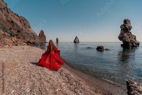 Beautiful sensual woman in a flying red dress and with long hair, stands on the seashore