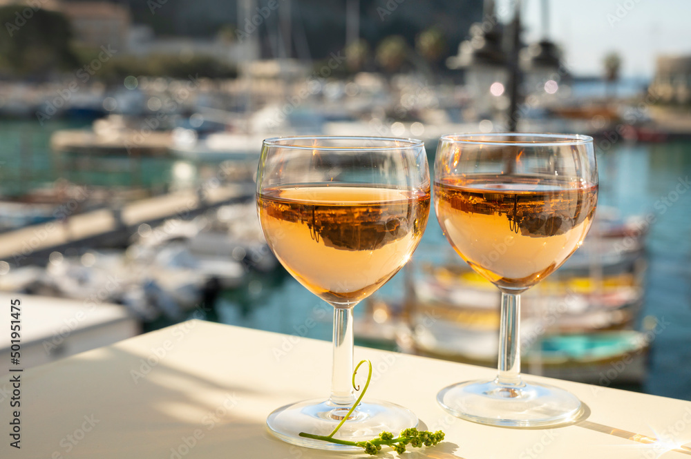 Obraz premium Summer party with cold rose wine in glass served on outdoor terrace in sunlights with view on old fisherman's harbour with colourful boats in Cassis, Provence, France