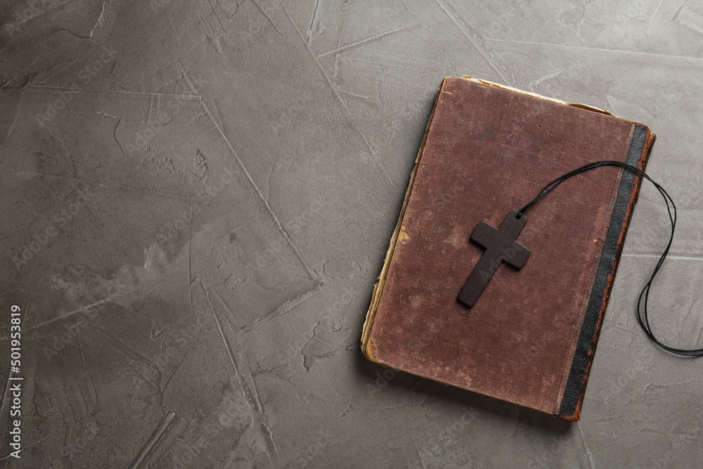 Wooden Christian cross and old Bible on grey table, top view. Space for text