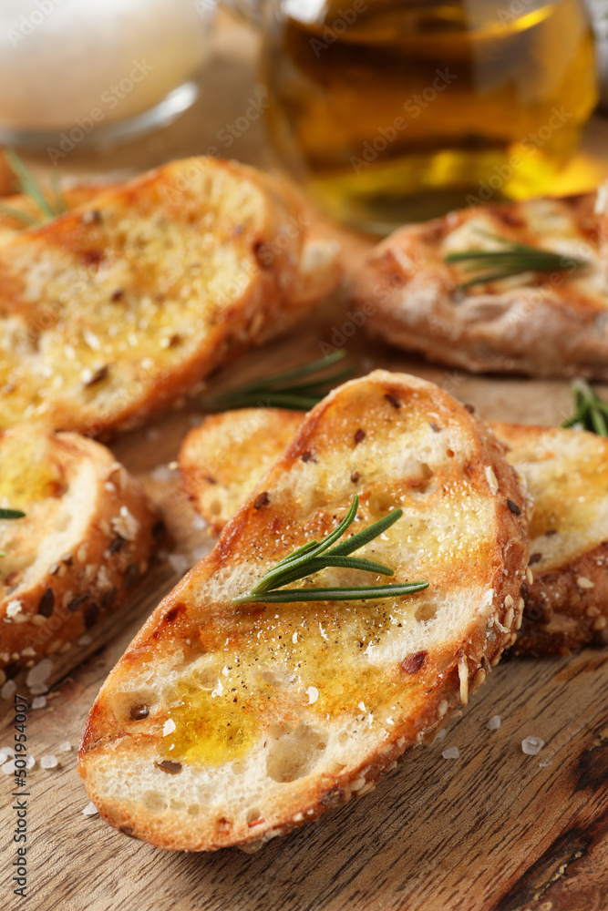 Tasty bruschettas with oil and rosemary on wooden board, closeup