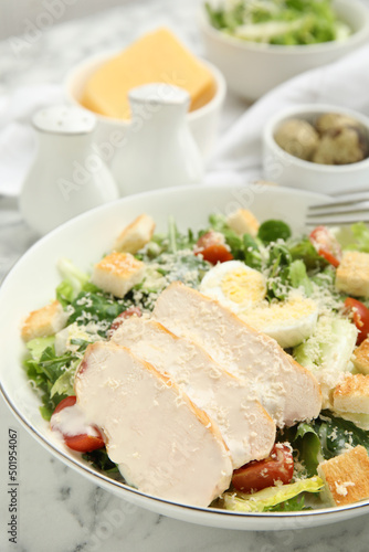 Delicious Caesar salad in bowl on white marble table, closeup