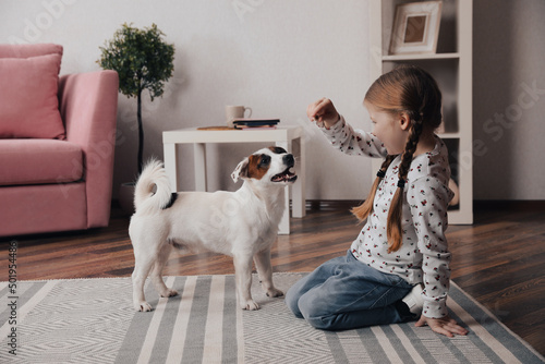 Cute little girl feeding her dog at home. Childhood pet Fototapet