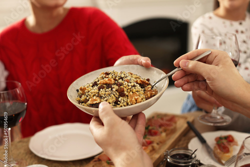 Man giving bowl of traditional Christmas kutia to woman at festive dinner indoors, closeup. Slavic dish